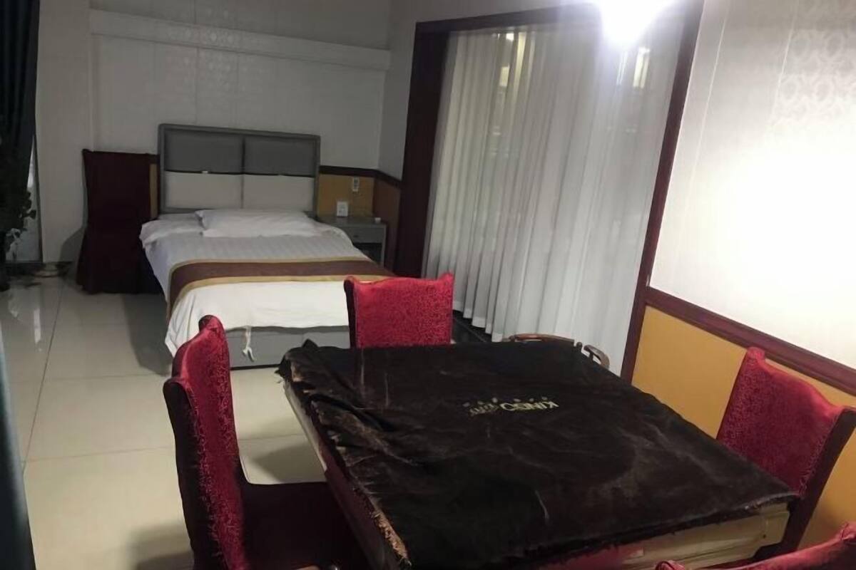 Una habitación de hotel con cama, una mesa con sillas, una mesita de noche y un ventanal con cortinas.