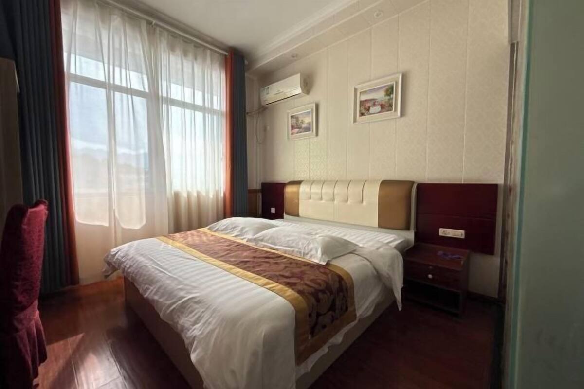 Habitación de hotel con una cama grande, una mesita de noche, una silla y una ventana con cortinas.