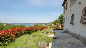 A stone pathway leading to a building with a view of the sea and hills.