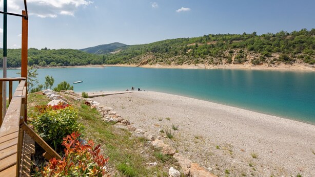 A beach with a wooden deck and a view of a calm lake surrounded by hills.