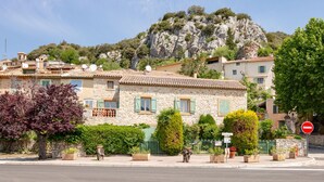 A stone building with a tiled roof, surrounded by greenery and a mountain backdrop.