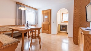 Een gezellige kamer met een houten eettafel, stoelen, een bank en een kitchenette.