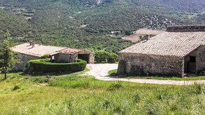 Ein ländliches Dorf mit traditionellen Steinhäusern, einem unbefestigten Weg und sanften, grünen Hügeln im Hintergrund.