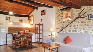 Ein gemütlicher Wohnbereich mit Steinwand, Holzboden, einem Esstisch mit Stühlen, einer Couch und einer Lampe.