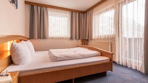 A hotel room with a wooden bed, a nightstand, a window with curtains, and a radiator. - Apart Romantica by Interhome (Kappl)
