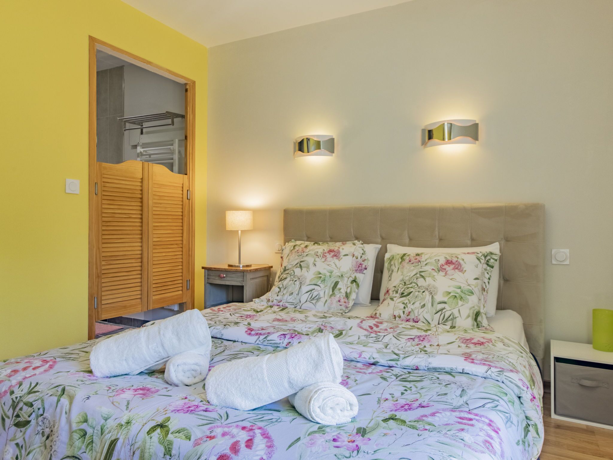Une chambre à coucher avec une couvre-lit à motifs floraux, deux lampes de chevet, une armoire en bois et une table de chevet avec une lampe.