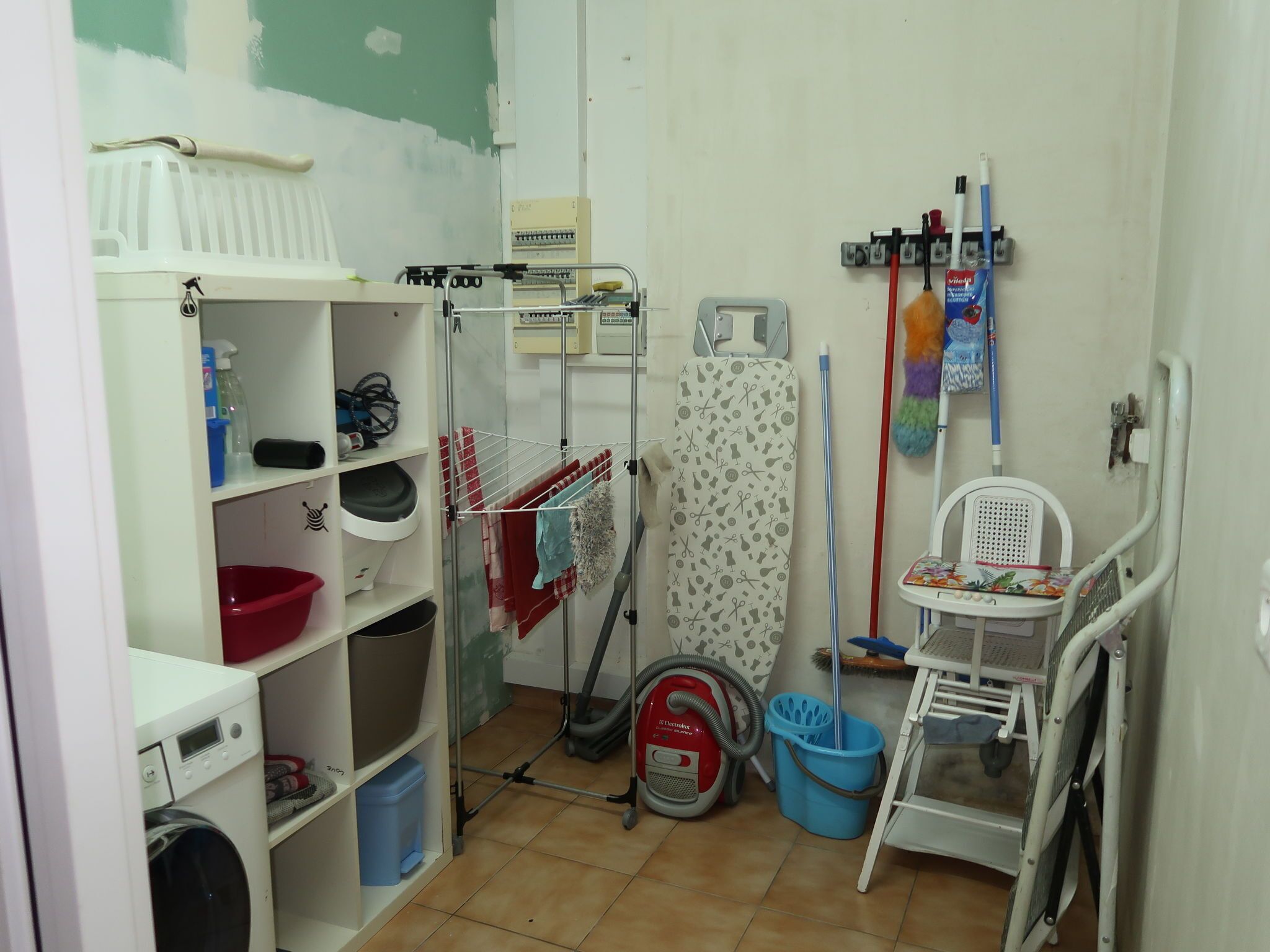 Une buanderie équipée d’un lave-linge, d’un étendoir, d’un aspirateur et d’une planche à repasser.
