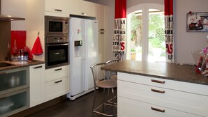 A modern kitchen with white cabinetry, stainless steel appliances, a bar stool, and a view of the outdoors through a glass door. - Sweet Home in Luberon by Interhome (Villelaure)