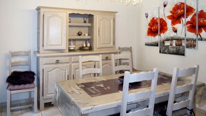 A dining area with a table covered in a tablecloth, surrounded by white chairs. There is a chandelier above the table and a painting of flowers on the wall. - Sweet Home in Luberon by Interhome (Villelaure)