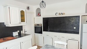 A compact kitchen with white cabinetry, a black backsplash, a built-in oven, and a dining area with a table and chairs. - Vacation home Kasara by Interhome (Mazan)