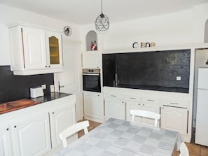 A compact kitchen with white cabinetry, a black backsplash, a built-in oven, and a dining area with a table and chairs.