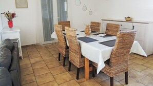 A dining area with a table set for four, surrounded by wicker chairs, a grey sofa, and a white cabinet. - Vacation home Kasara by Interhome (Mazan)