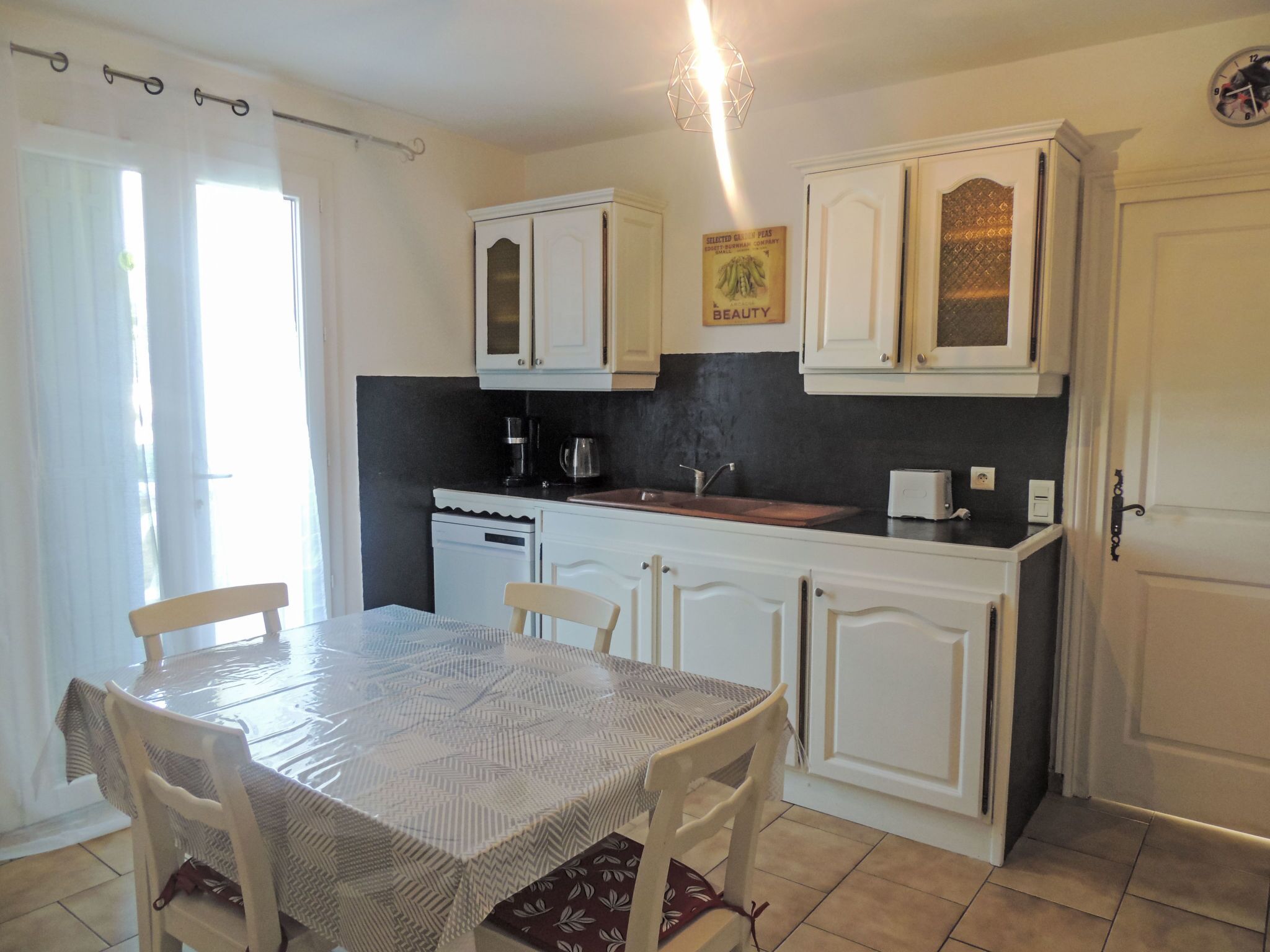 A kitchen with white cabinets, a dining table with chairs, a coffee maker, and a clock on the wall.