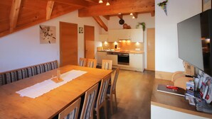 A cozy kitchen with wooden beams, a dining area with a wooden table and chairs, and a TV on a stand. - Bergblick by Interhome (Kappl)