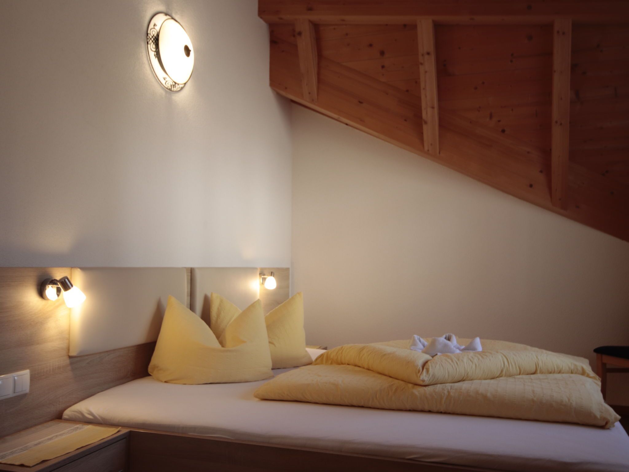 A bedroom with a bed, pillows, a nightstand, and wall-mounted lighting.