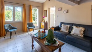 Ein Wohnzimmer mit einer Couch, zwei Sesseln, einem Couchtisch mit Getränken und einem Fenster mit Vorhängen.