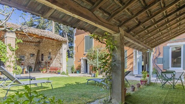 Un espace extérieur abrité, comprenant un bâtiment en pierre, une pelouse et du mobilier de jardin.