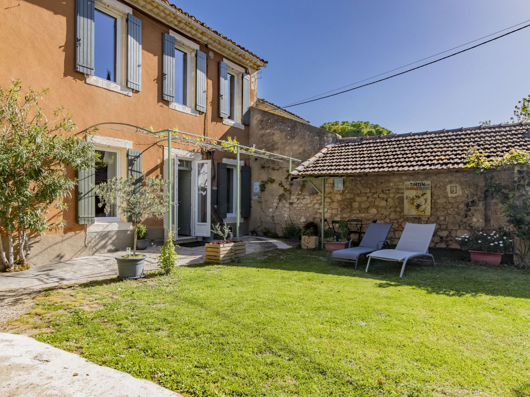 A two-story house with a garden, a pergola, and a stone wall.
