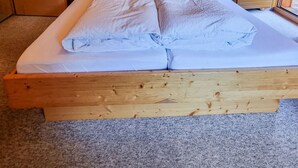 Een houten kamer met een bed, houten plafond en een raam met uitzicht op bomen.