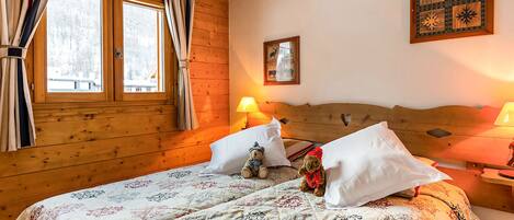 Una habitación acogedora con paredes de madera, una cama grande con ropa de cama estampada, dos lámparas de noche y un cuadro en la pared.