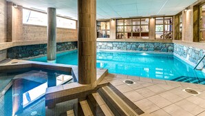 An indoor swimming pool with stone walls and wooden beams, surrounded by tiled flooring and a stone ledge.