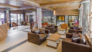 A spacious lobby with leather sofas, wooden coffee tables, and a stone fireplace.
