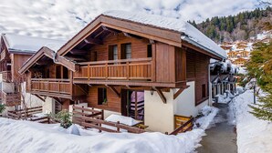 A wooden chalet with a balcony and a snow-covered path leading to it.