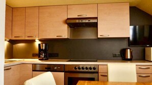 A compact kitchen with wooden cabinets, a stainless steel range hood, a coffee maker, and a kettle. - Apartment Selina by Interhome (Kappl)