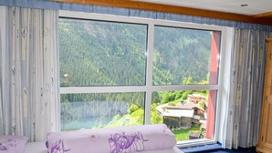 A room with a large window offering a view of a forested mountain area. - Apartment Selina by Interhome (Kappl)