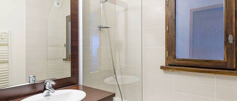 A bathroom with a white sink, a mirror, and a shower enclosure.
