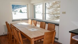 Ein Essbereich mit Holztisch und -stühlen, großen Fenstern mit Blick auf einen verschneiten Berg und einem Heizkörper an der Wand.