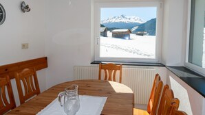 A dining area with a wooden table, chairs, a pitcher of water, and a window with a snowy mountain view. - Altes Zollhaus by Interhome (Nauders)