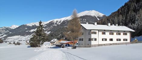 A snow-covered landscape with a building featuring multiple windows and a snow-covered roof.