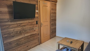 A room with a wooden wall, a television mounted above a door, and a small table with a remote control. - Apartment Köhle by Interhome (Pfunds-Samnaun)