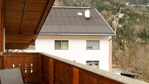 Uma varanda com mesa e cadeiras, com vista para uma casa e uma paisagem montanhosa.