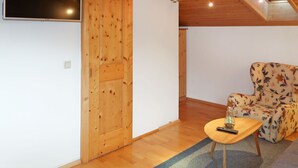 Um quarto acolhedor com teto de madeira, televisão na parede, porta de madeira e uma cadeira com padrão floral.