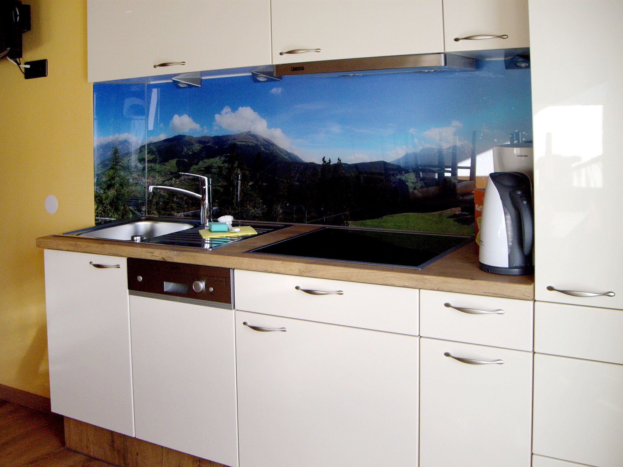 Una cocina con un lavabo, una cafetera y un armario con una ventana sobre el lavabo.