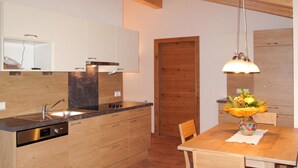A modern kitchen with wooden cabinets, a built-in dishwasher, and a wooden dining table with chairs. - Alpenherz by Interhome (Prutz/Kaunertal)