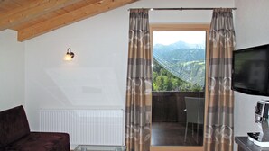 A living room with a glass coffee table, a dark-colored sofa, a television, and a view of mountains through a sliding glass door. - Alpenherz by Interhome (Prutz/Kaunertal)