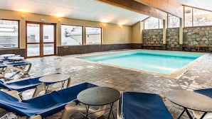 Un área de piscina interior con pared de piedra, techo de madera y suelo de baldosas.