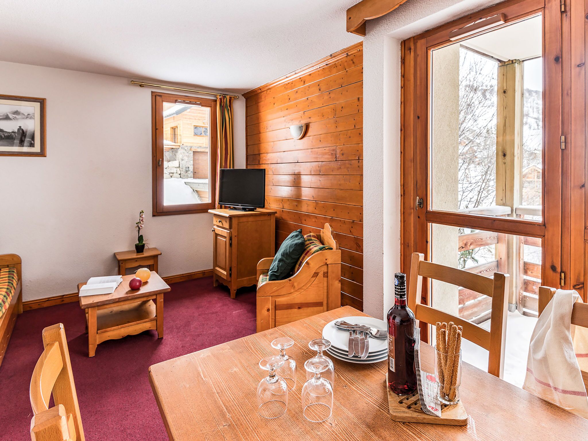 Una habitación acogedora con paredes de madera, una mesa de comedor con vasos y cubiertos, un televisor y un ventanal con vistas a árboles.