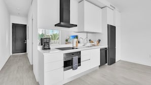 A modern kitchen with white cabinetry, a black range hood, a built-in oven, a refrigerator, and a coffee maker. - Modern 1BR | Pool & BBQ | Steps to 7 Mile Beach (Grand Cayman)