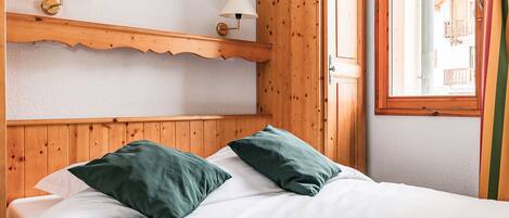 A wooden cabin room with a bed, two wall-mounted lamps, and a window with curtains.
