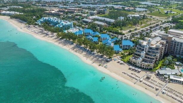 An aerial view of a coastal resort with beachfront villas, a sandy beach, and clear turquoise waters.