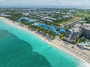 An aerial view of a coastal resort with beachfront villas, a sandy beach, and clear turquoise waters.