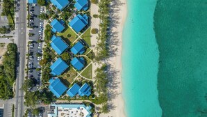 An aerial view of a coastal hotel with multiple blue-roofed buildings, a parking lot, and a beach.
