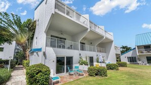 A two-story building with balconies, a patio area with chairs, and a well-maintained lawn.