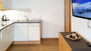 A modern kitchen with white cabinets, a dishwasher, and a sink. A television mounted on the wall displays a snowy mountain scene. - Apartment Walch by Interhome (Prutz/Kaunertal)