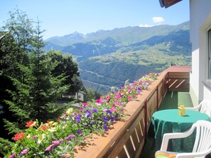 A balcony with a wooden railing, a table with a green tablecloth, and a chair. - Apartment Walch by Interhome (Prutz/Kaunertal)