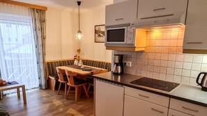 A compact kitchen with a microwave, stove, and coffee maker. There is a dining area with a table and chairs. - Apartment Walch by Interhome (Prutz/Kaunertal)